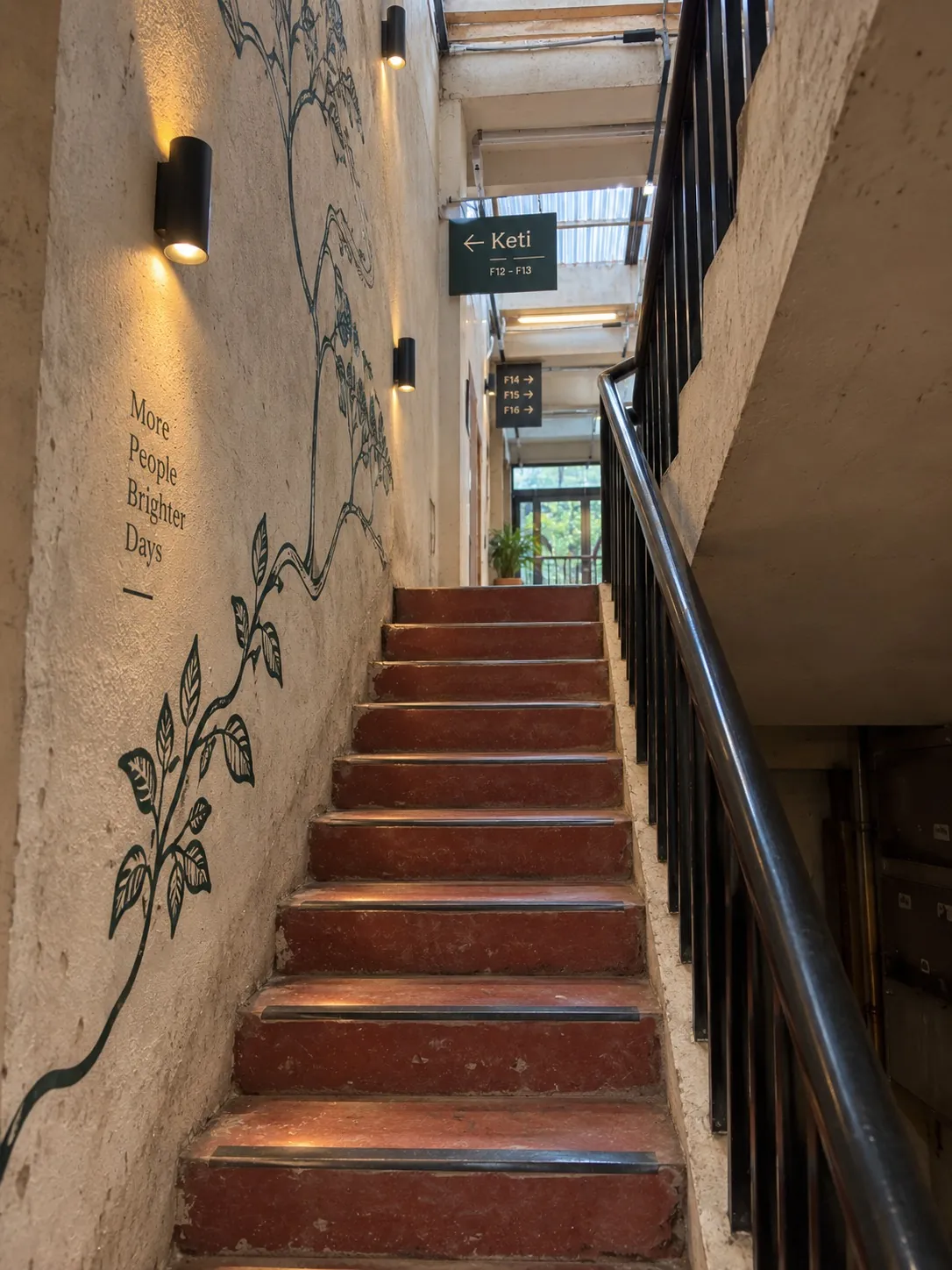 Keti concept: the stair with warm wall lights, a tree mural and a sign reading Keti, F12 to F13